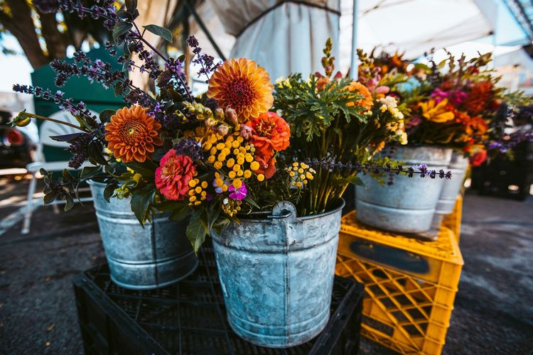 Colorful flowers in galvanized buckets on a rustic table, with orange crates in a market stall