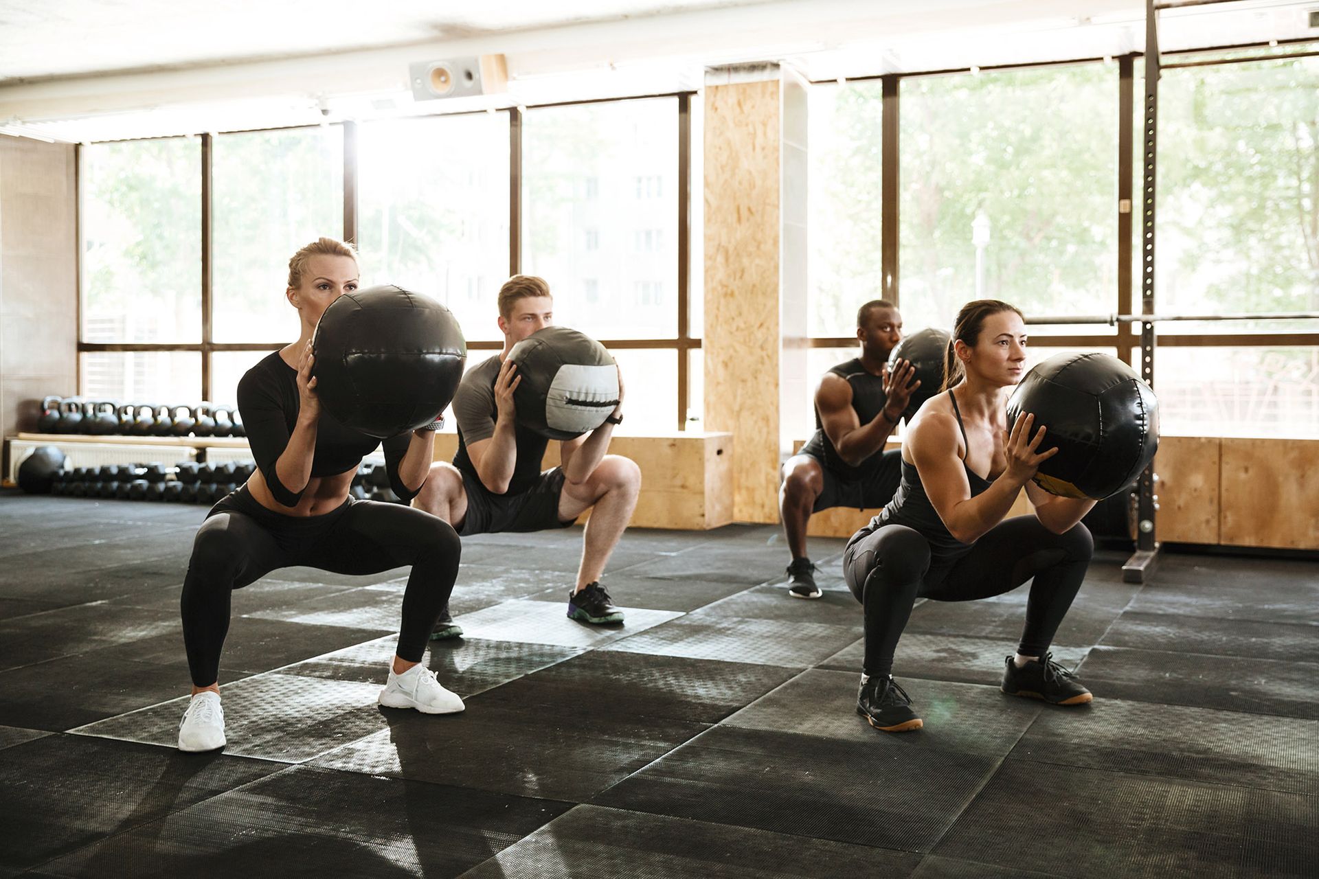 People in gym doing weighted squats, holding medicine balls.