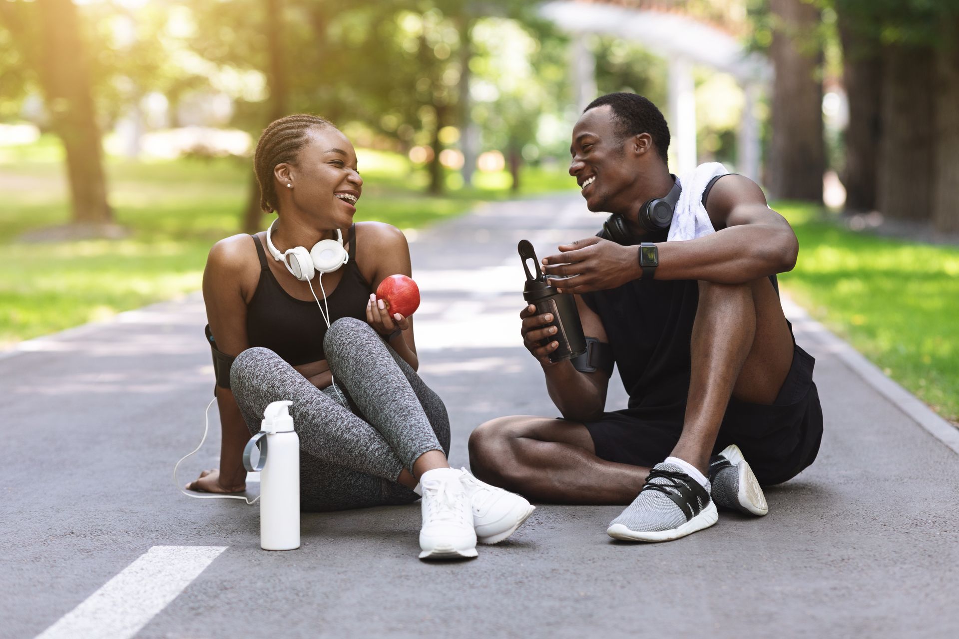 Two people rest on a path after a workout, smiling and laughing.