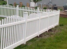 A white picket fence surrounds a lush green yard in front of a house.