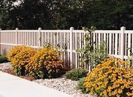 A white fence surrounds a garden with yellow flowers.