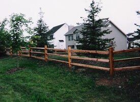 A wooden fence surrounds a lush green field in front of a house.