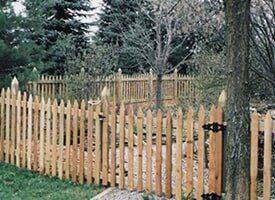 A wooden picket fence is surrounded by trees in a yard.