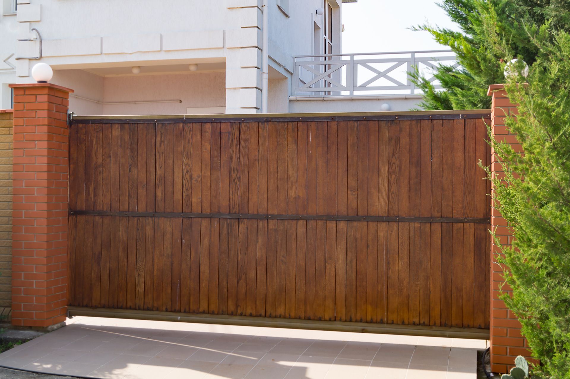 A wooden sliding gate is open to a driveway in front of a house.