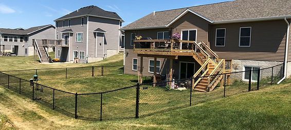 A large house with a deck and stairs is surrounded by a chain link fence.