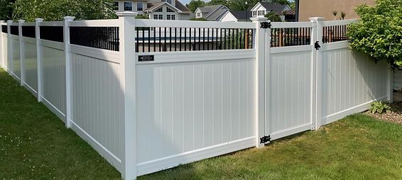 A white vinyl fence with a black gate in a backyard.