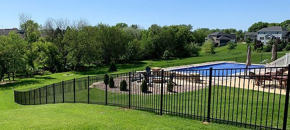 A black fence surrounds a swimming pool in a backyard.
