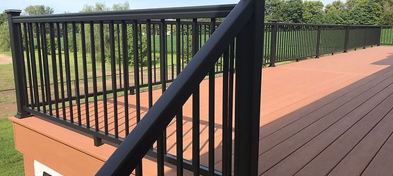 A wooden deck with a black railing and stairs leading up to it.