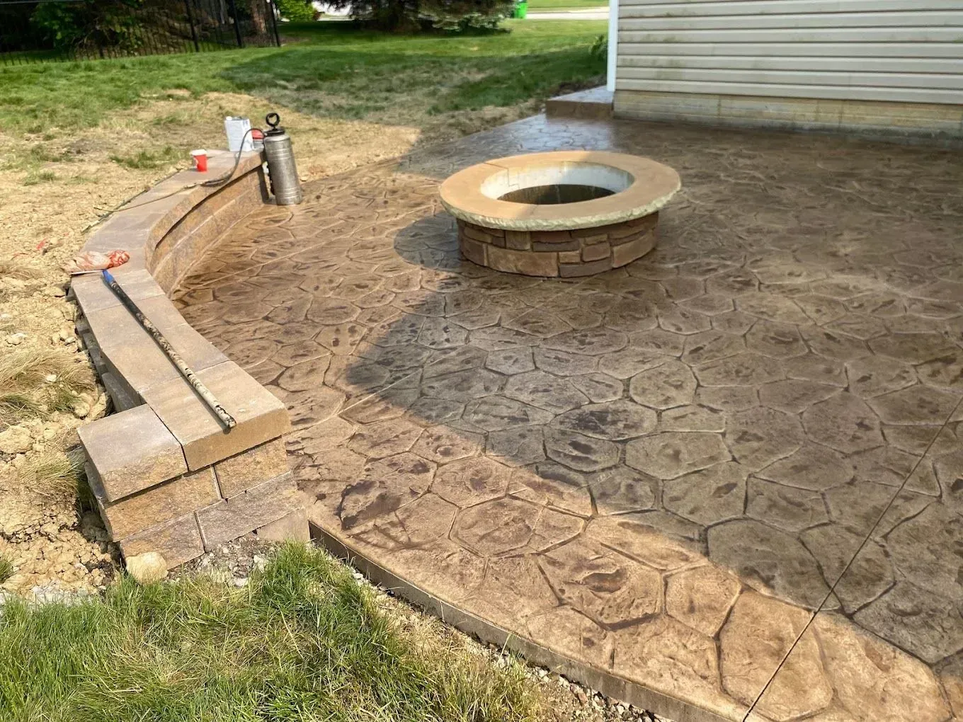 Backyard patio with stamped concrete, curved brick edging, and a circular fire pit near a house