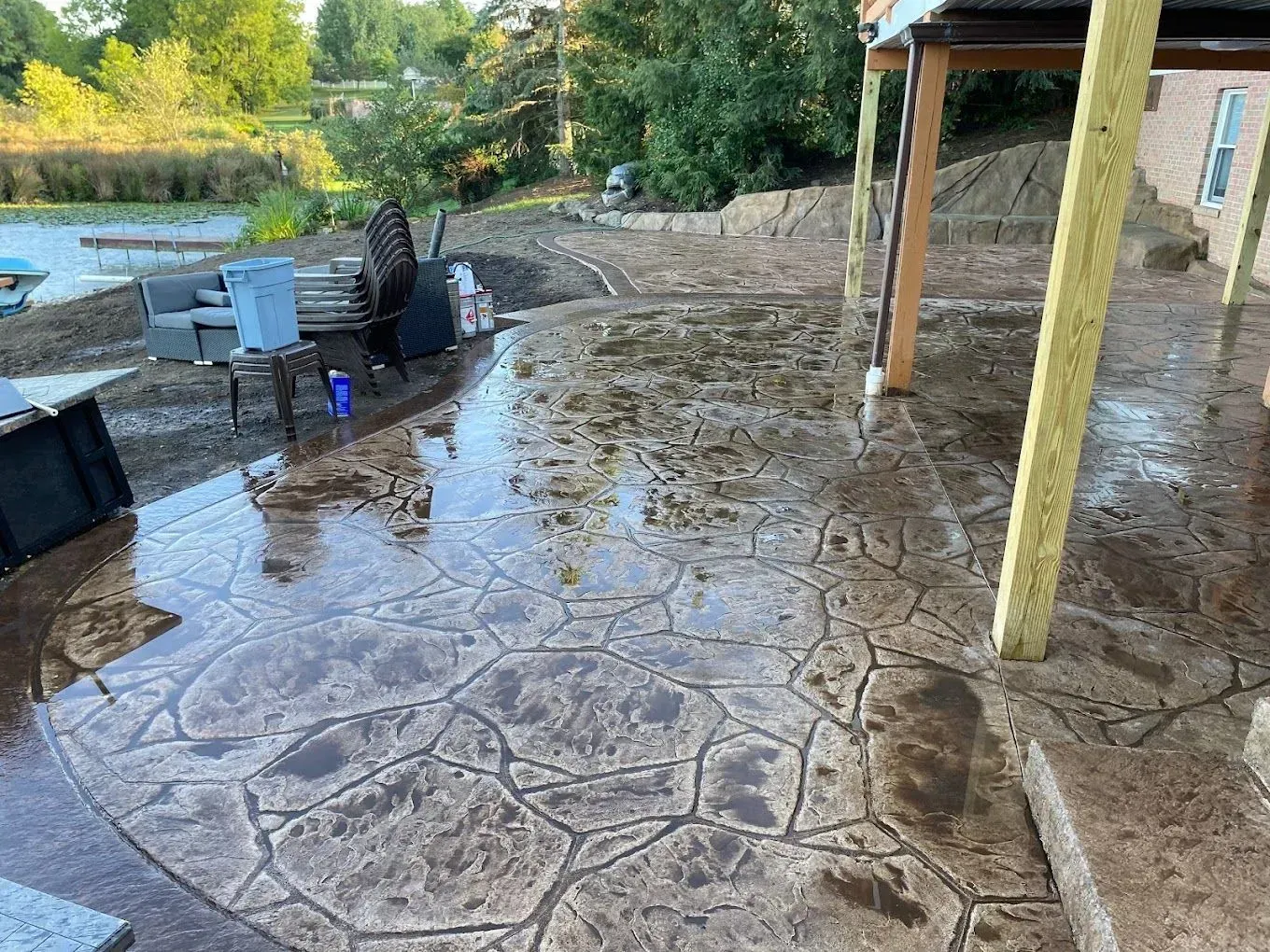 Rain-soaked stamped concrete patio with outdoor furniture and a pool in the background