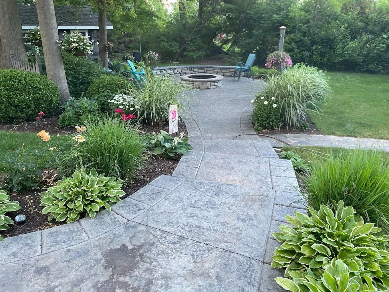 Curved stone garden path leading to a patio with lush green shrubs and trees