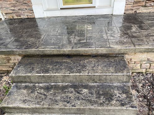 Stone front steps leading to a white door with a wet, weathered patio above