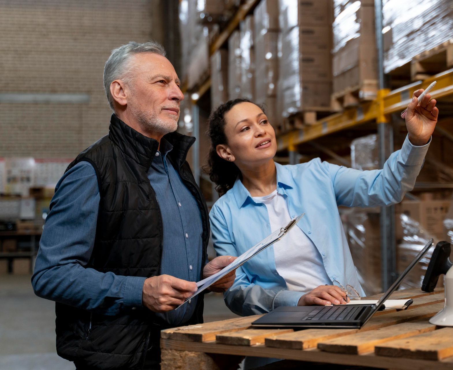 A man and a woman are looking at a laptop in a warehouse.