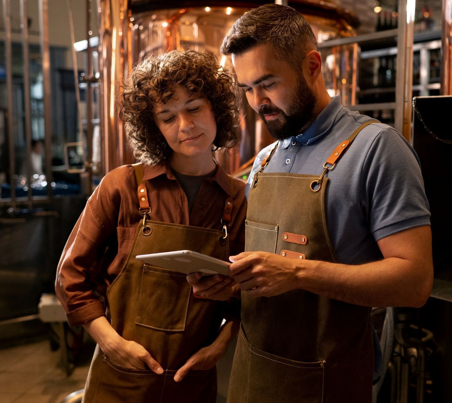 A man and a woman are looking at a tablet in a brewery.