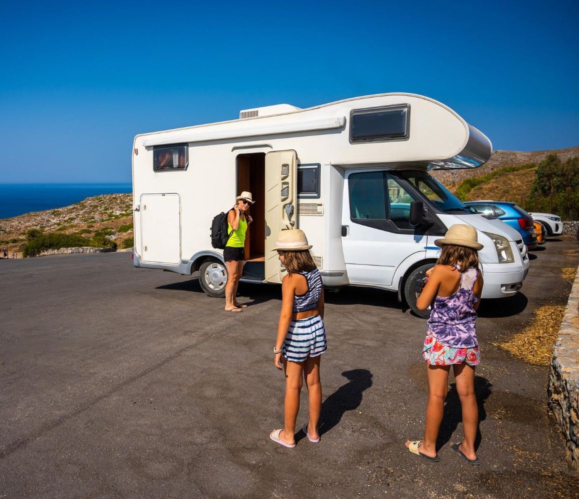 Two girls are standing in front of a rv parked on the side of the road.
