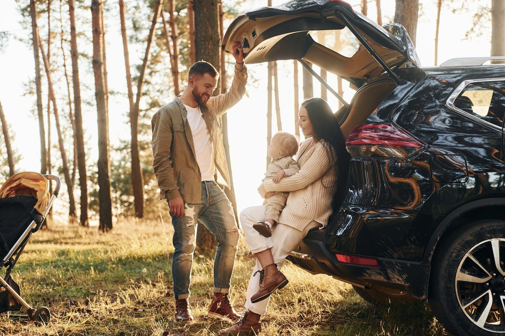 A family is sitting in the back of a car in the woods.