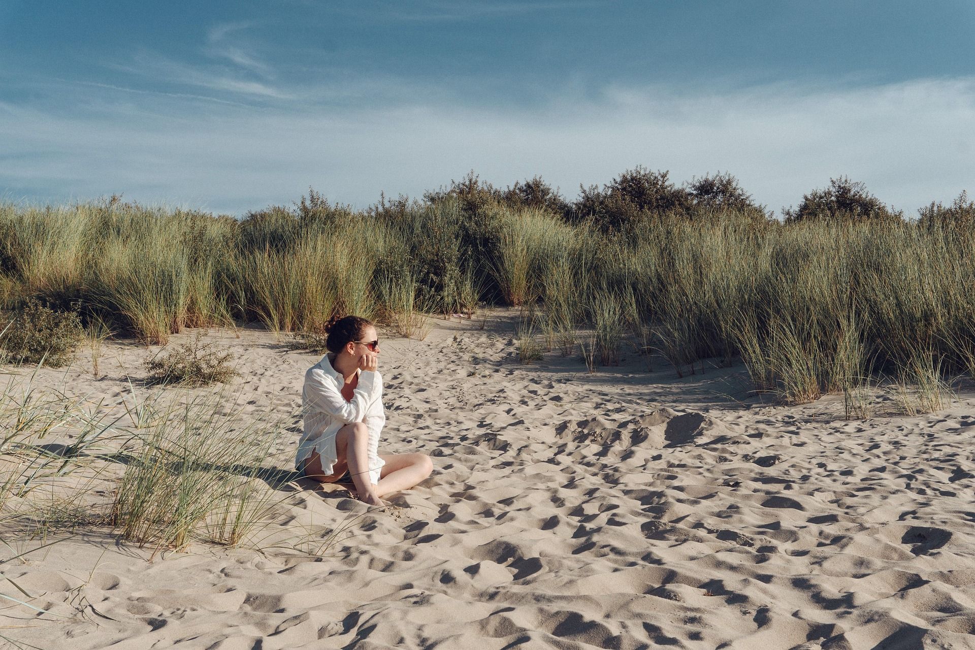 A woman is sitting on a sandy beach wearing sunglasses.