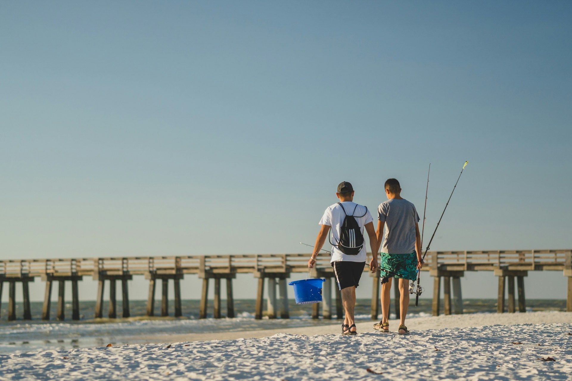 Two men are walking on the beach with fishing rods.