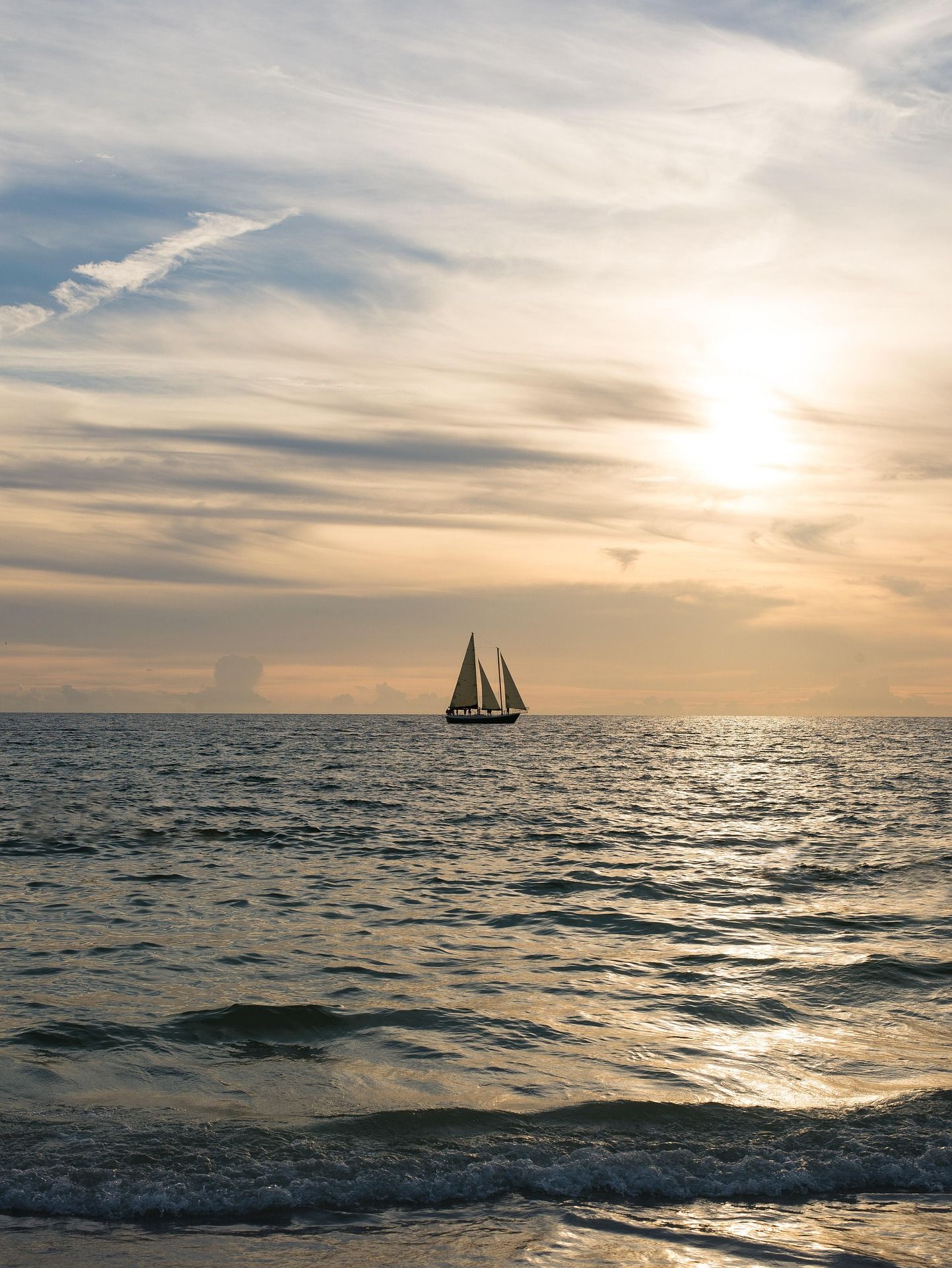 A sailboat is floating on top of a large body of water at sunset.