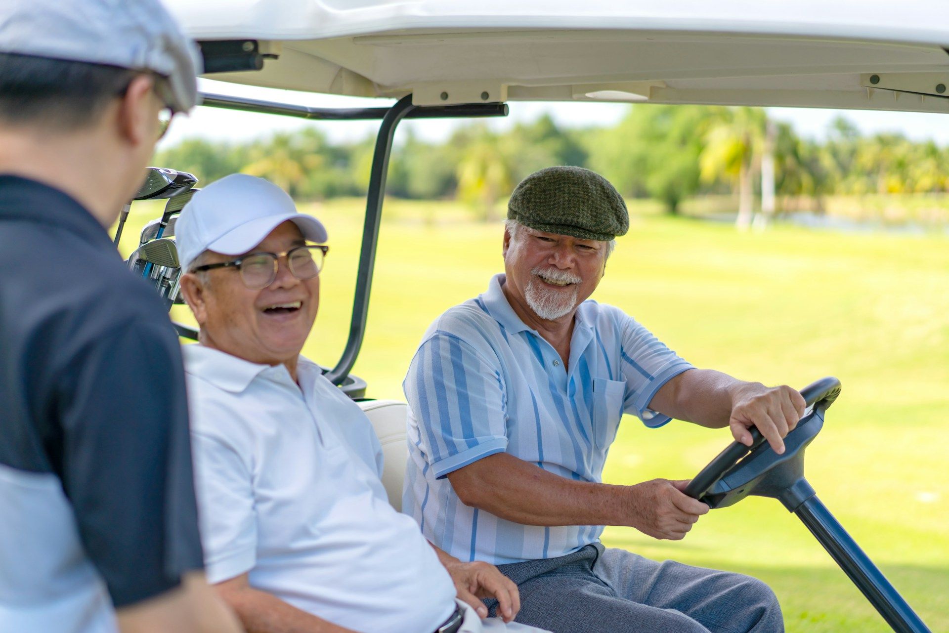 Three older men are sitting in a golf cart on a golf course.