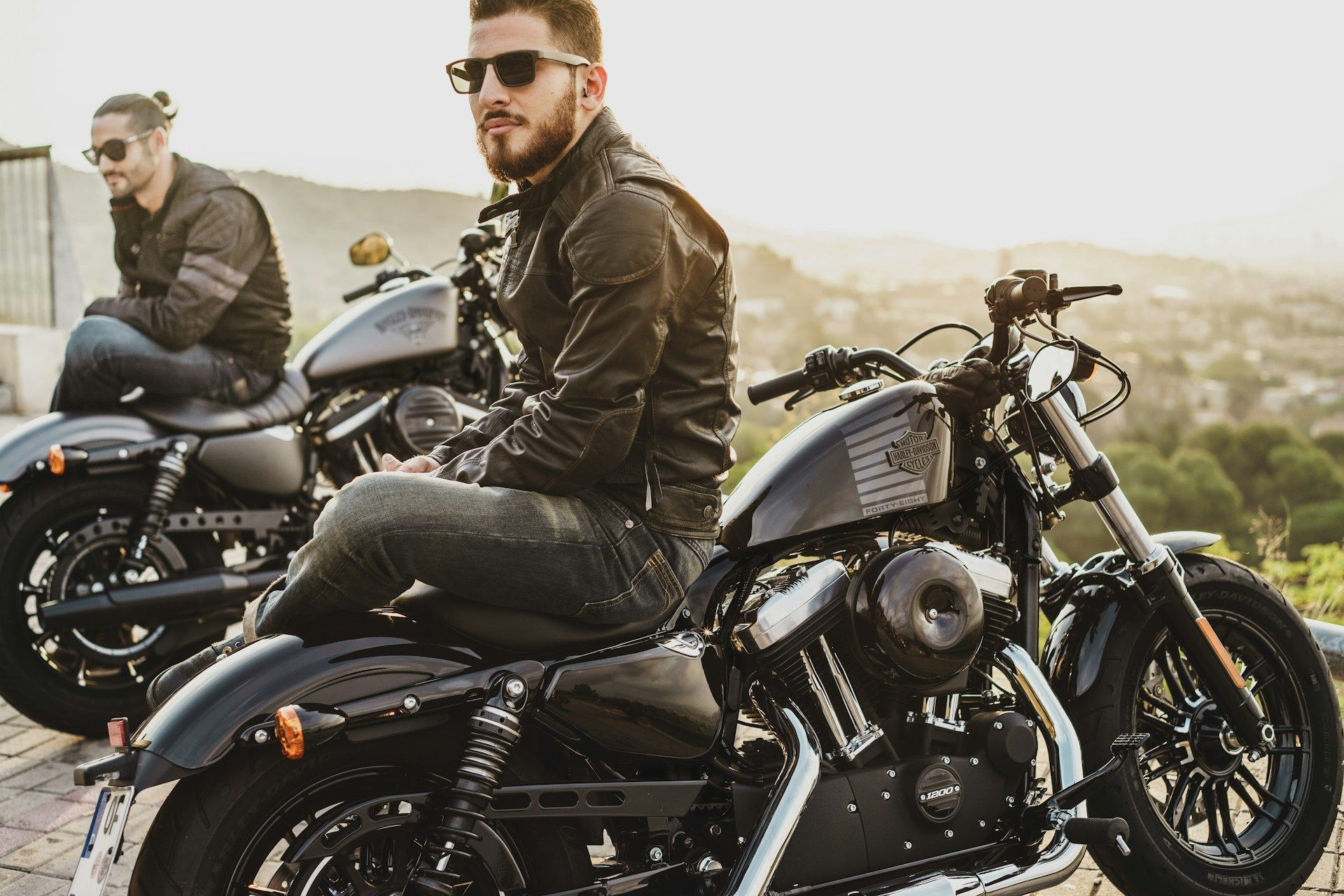 Two men are sitting on motorcycles on top of a hill.