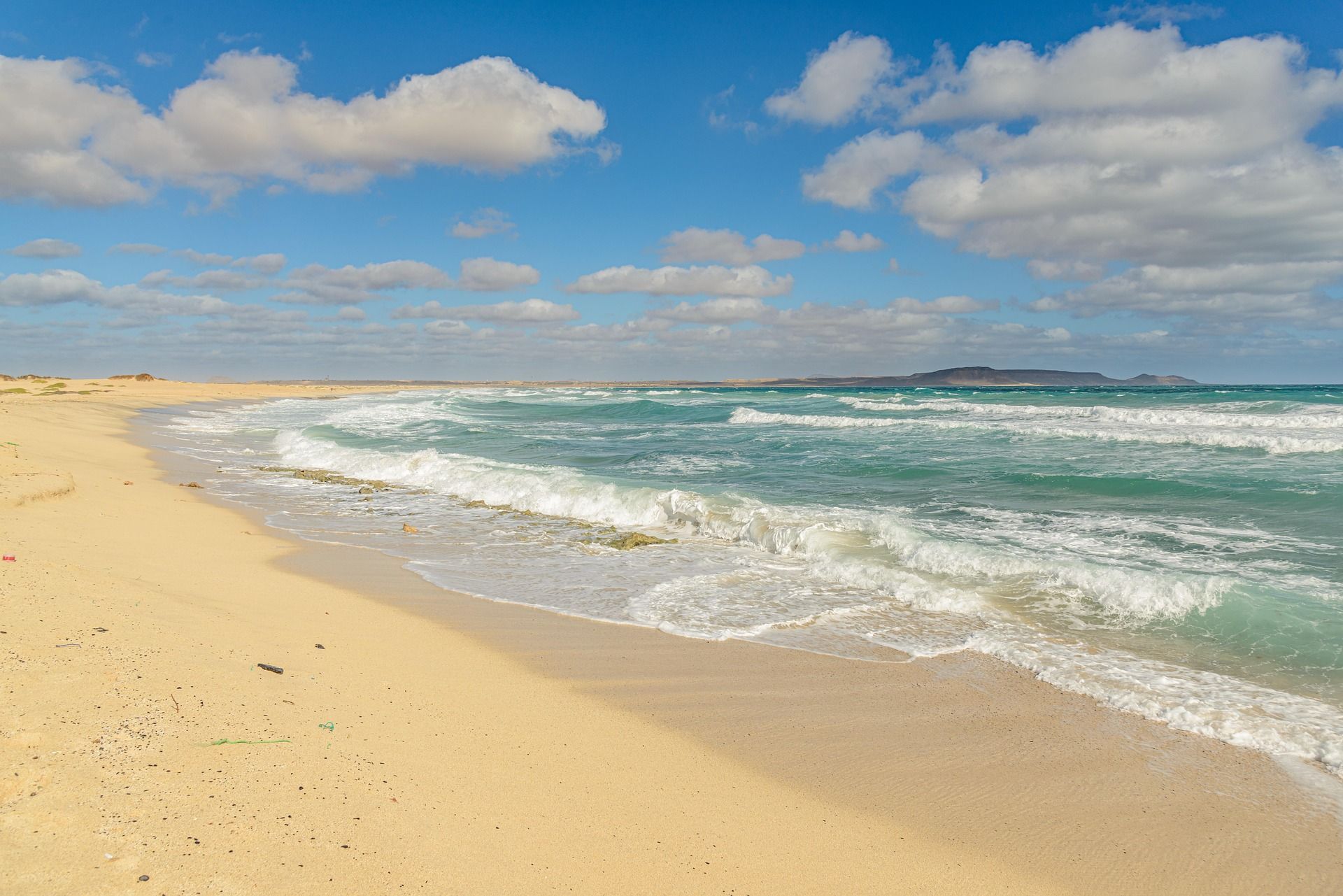 A sandy beach with waves crashing against the shore on a cloudy day.