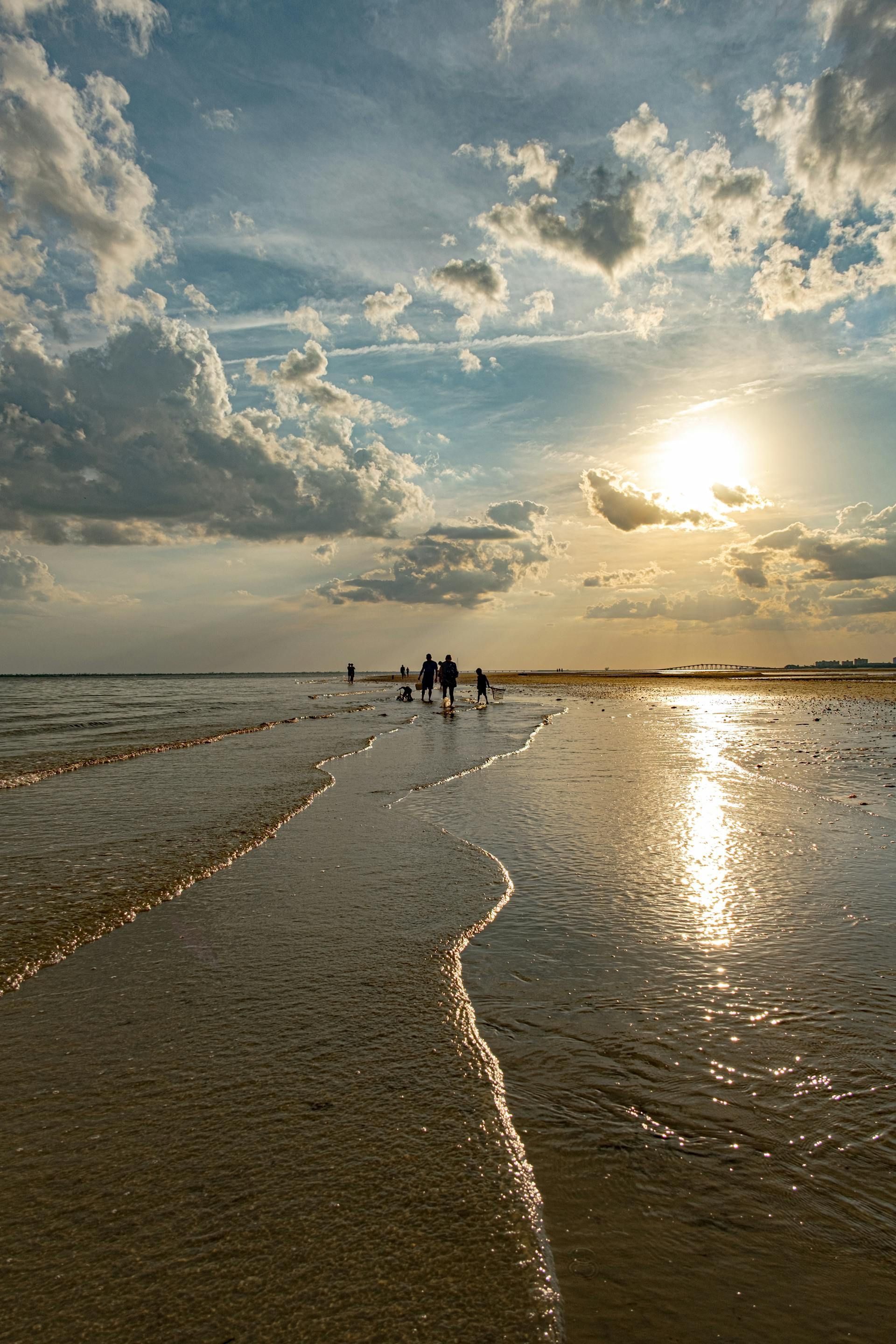 A group of people are walking on a beach at sunset.