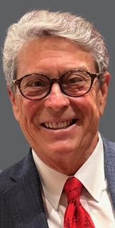 A man wearing glasses and a tie smiles for the camera
