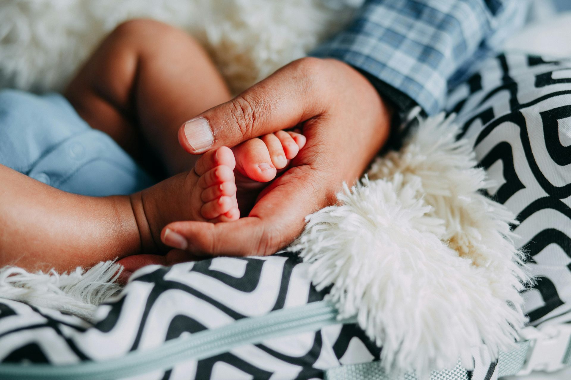 A hand holding a baby's tiny foot on a fluffy blanket.