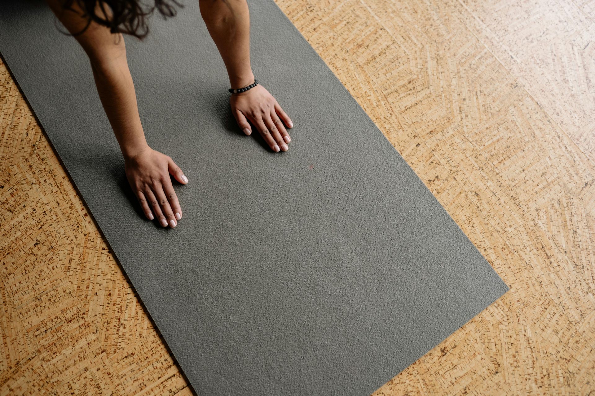 Hands on a gray yoga mat, with cork flooring in the background.