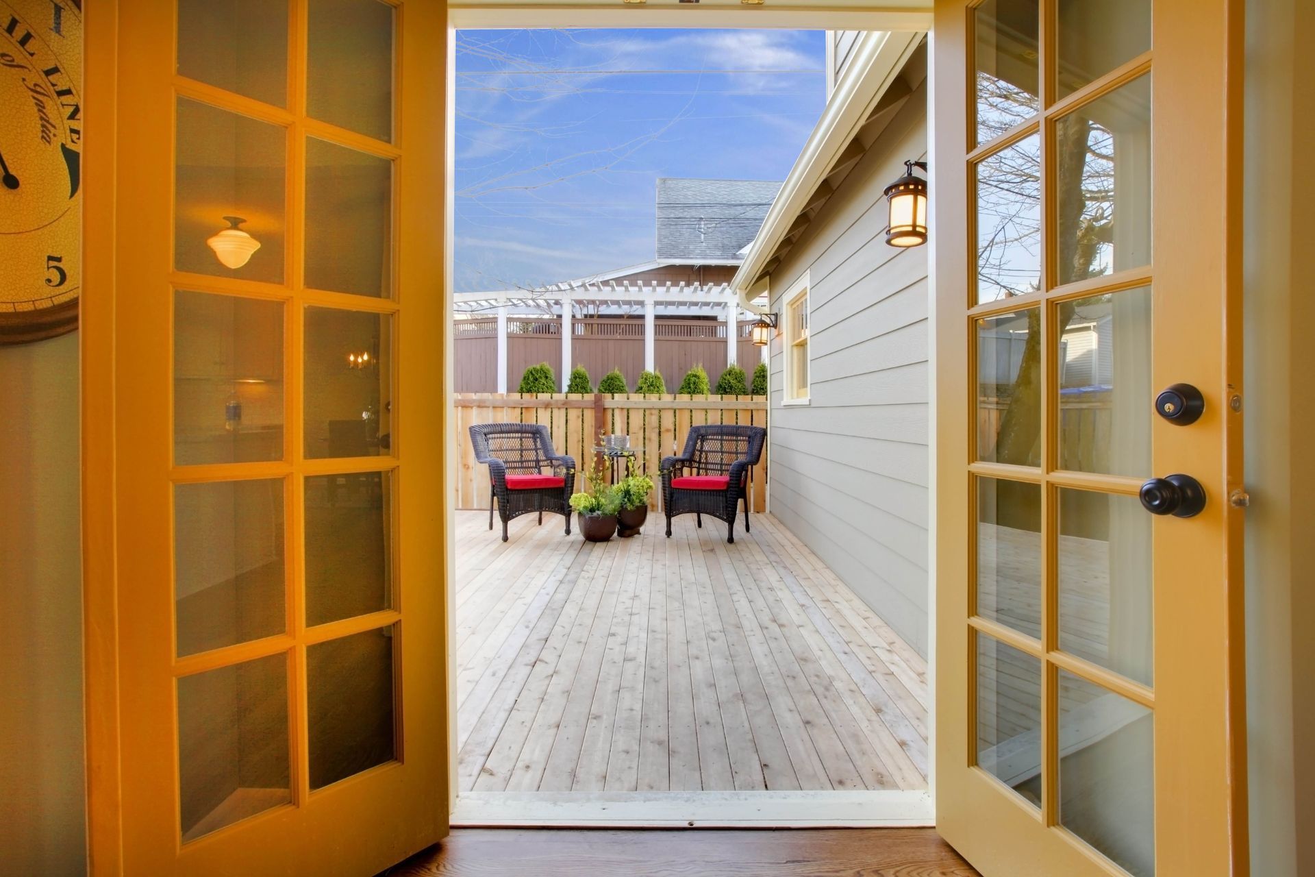 the french doors are open to a wooden deck with chairs and potted plants .