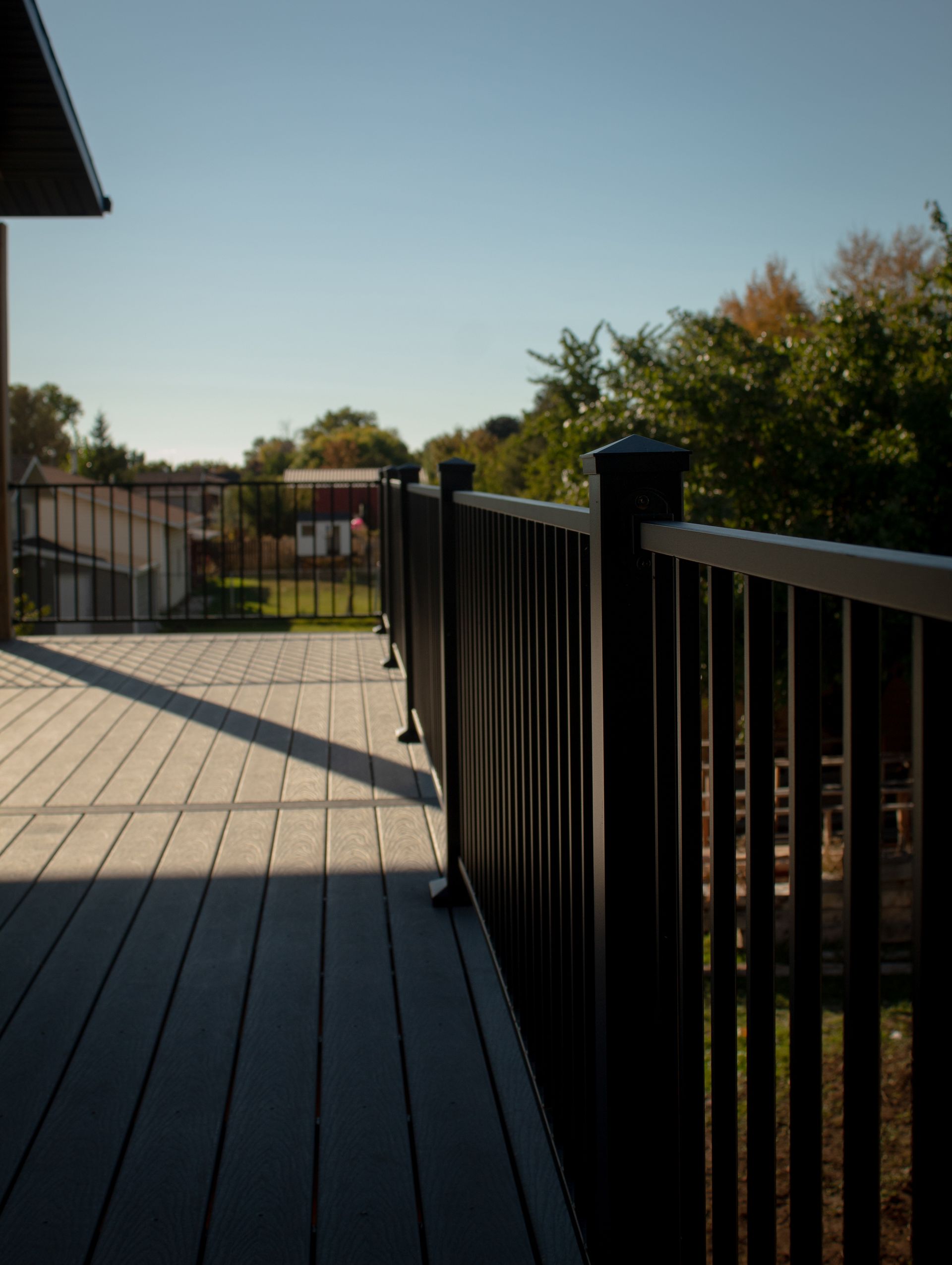 A deck with a black railing and a house in the background