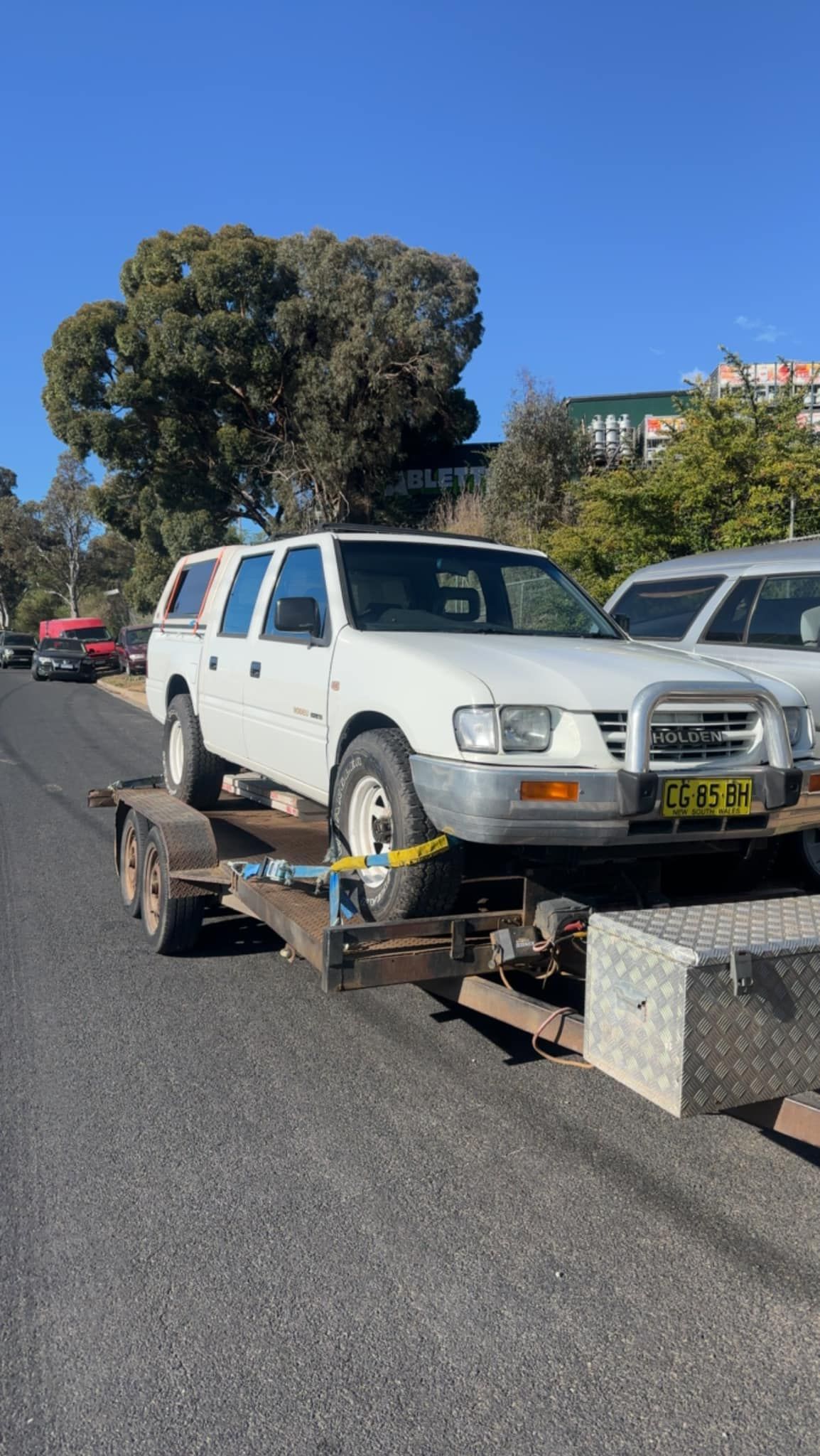 A White Truck Is Being Towed On A Trailer Down A Street — R N R Wrecking N Scrap Car Removal In Beard, ACT