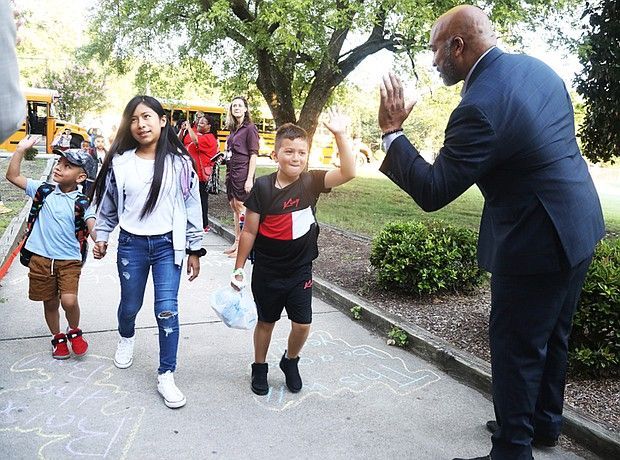A man in a suit is standing next to a group of children walking down a sidewalk.