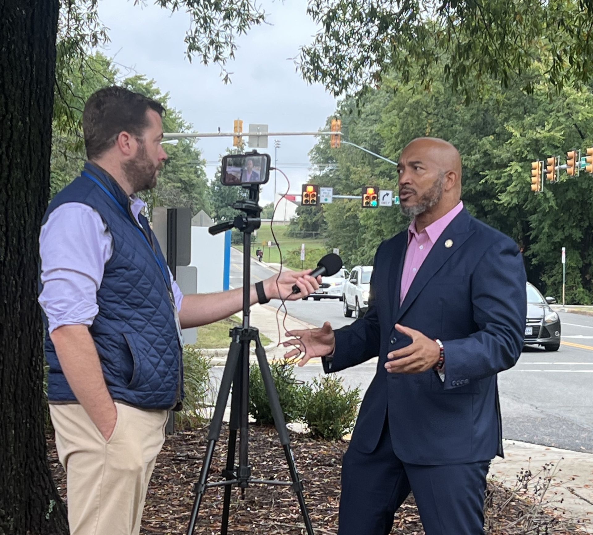 A man in a suit is talking to another man in a pink shirt