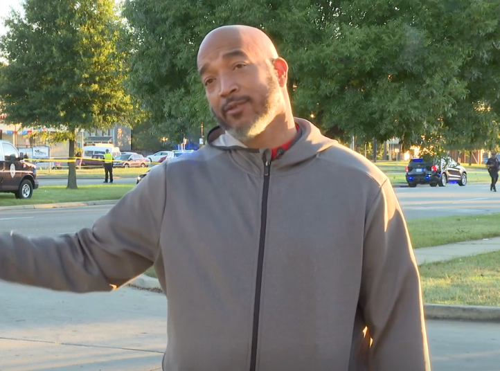 A man in a grey jacket is standing in a parking lot.