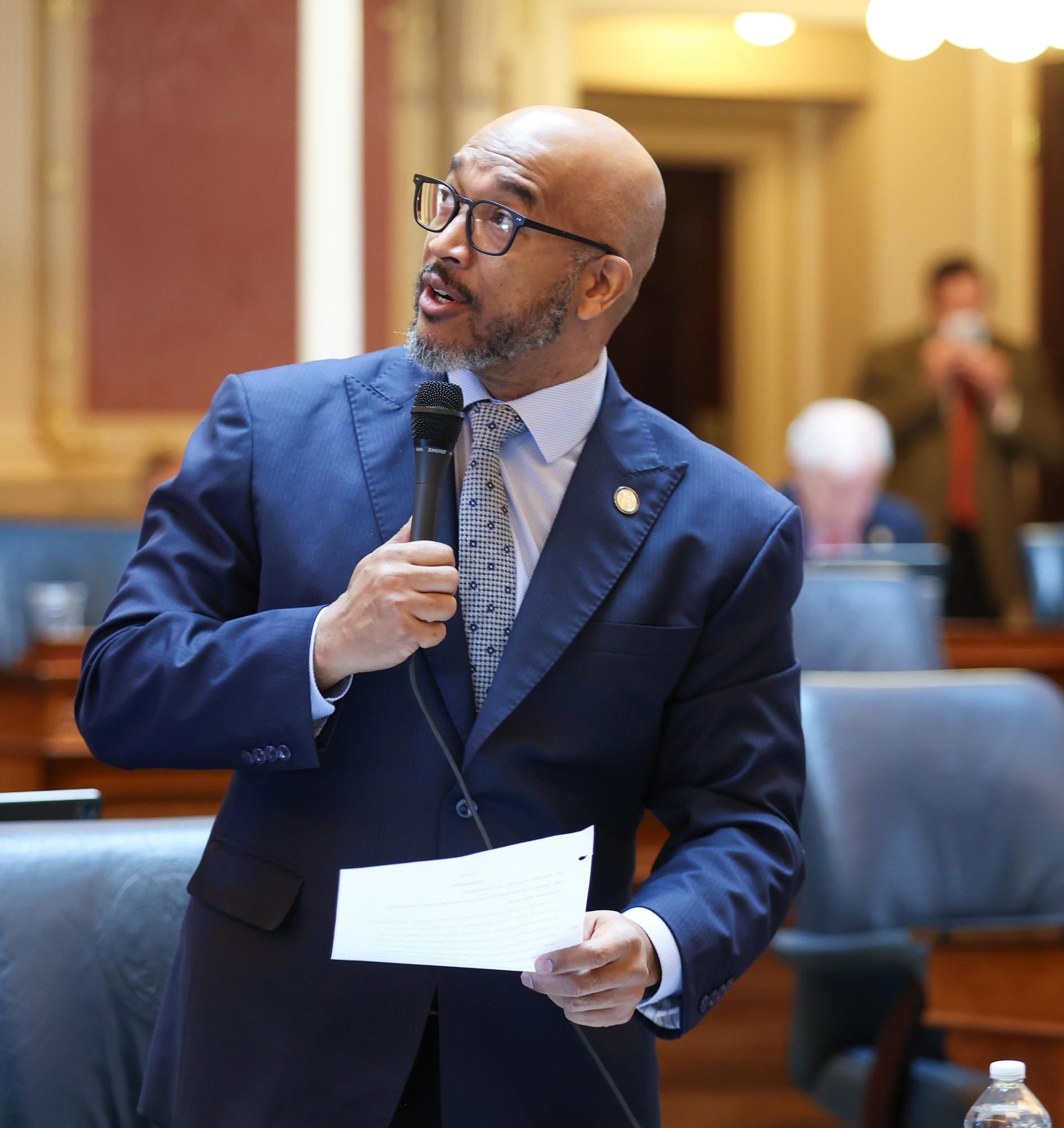 A man in a suit and tie is speaking into a microphone