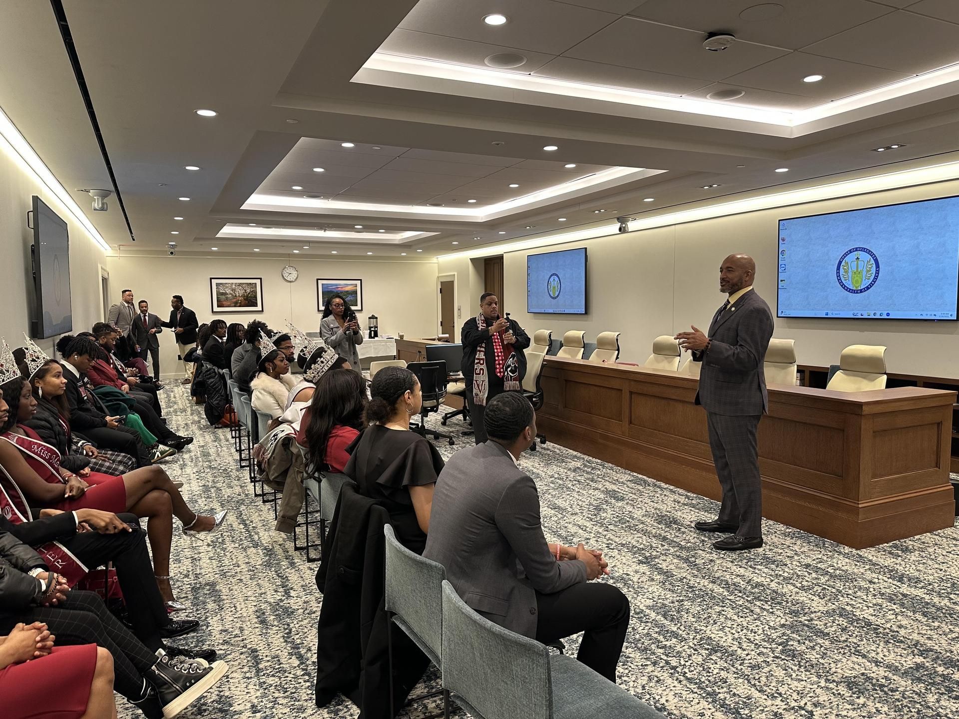 A man is standing in front of a large group of people in a conference room.