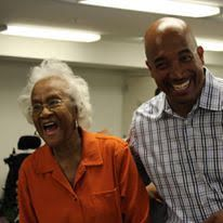 A woman in orange laughs with Delegate Mike Jones in a plaid shirt, both indoors.