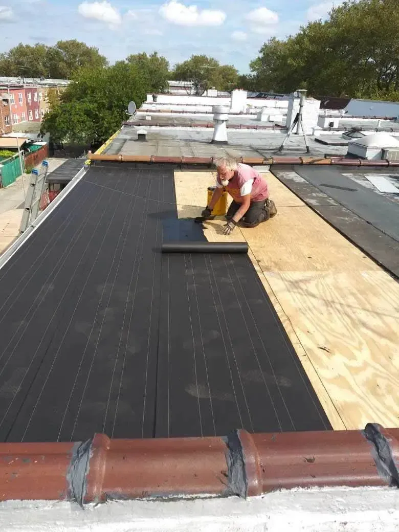 Roofer applying black roofing material to a plywood surface on a residential roof. 