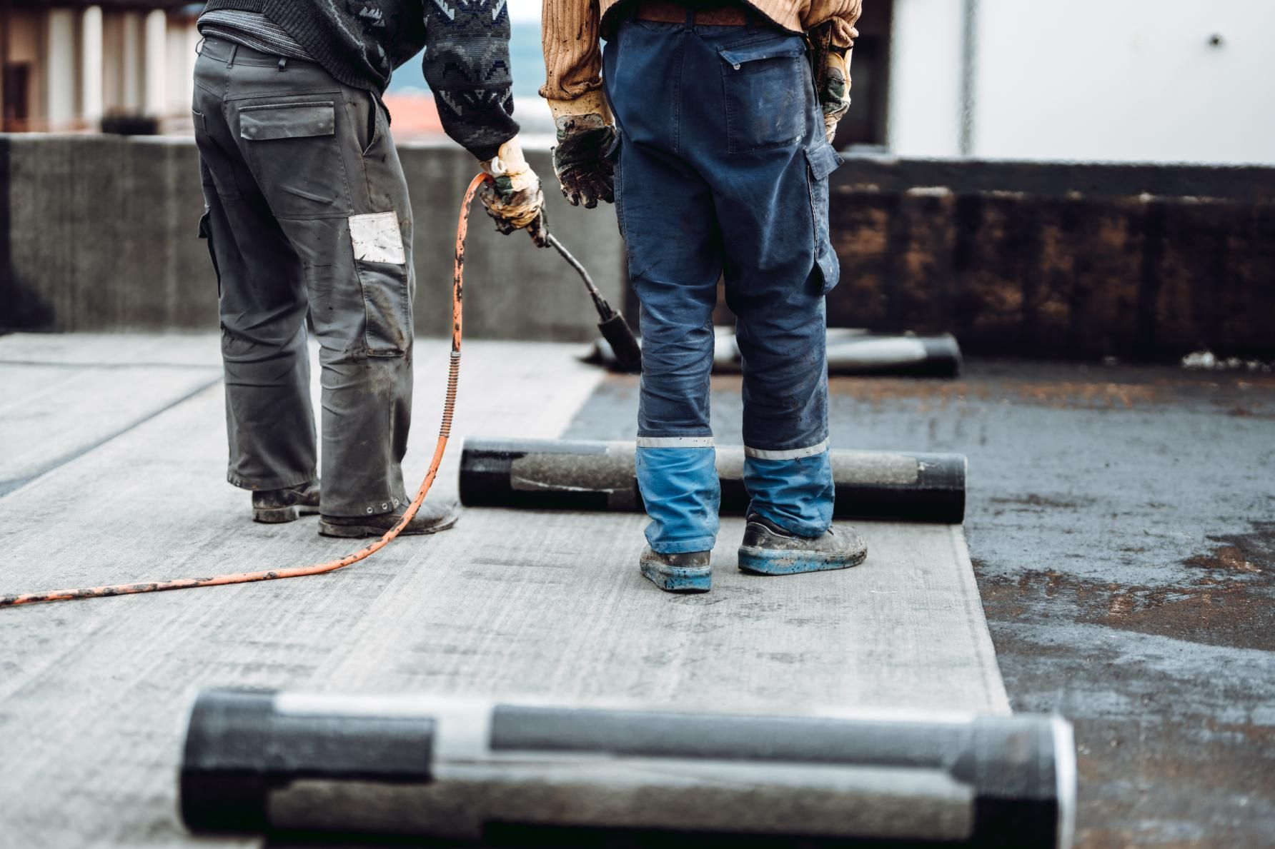 Two workers installing roofing material on a rooftop. 