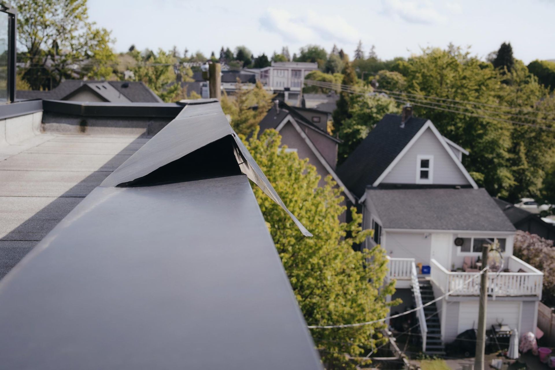 View from a rooftop looking over residential houses and trees on a sunny day.