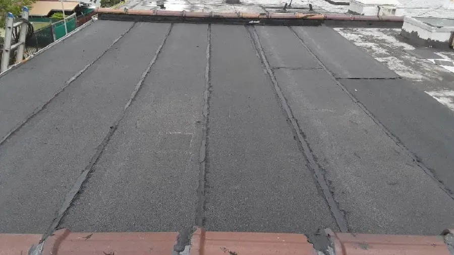 A flat roof with dark gray asphalt tiles, seen from above. 