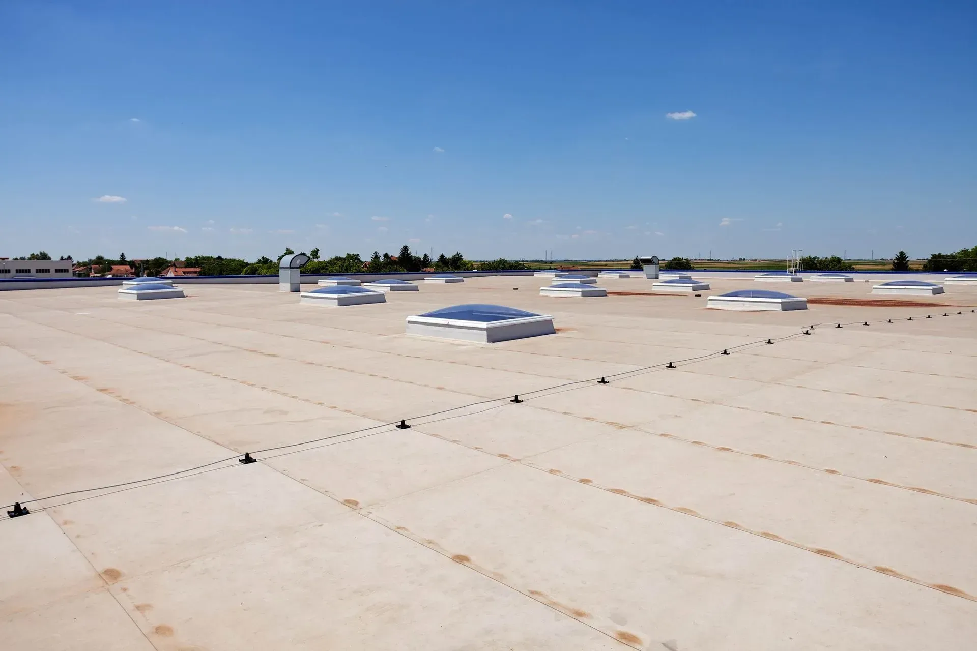 A wide, flat commercial roof with skylights under a clear blue sky.