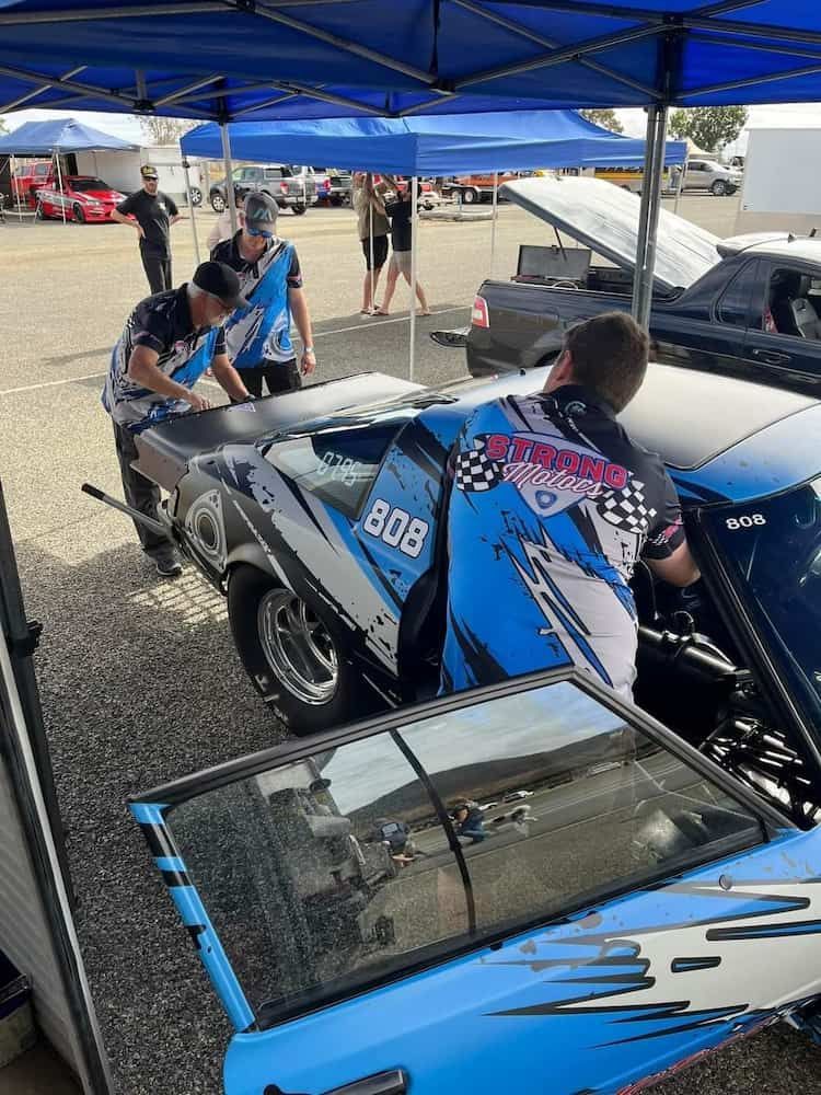 A Group Of Men Are Working On A Race Car In A Parking Lot — Strong Motors In Currajong, QLD