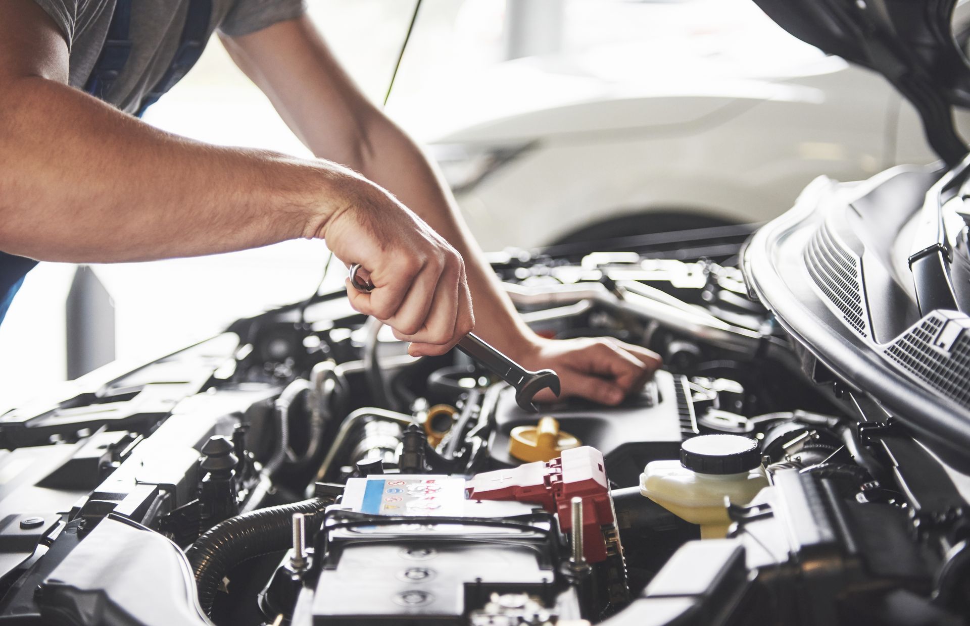 Technician with wrench in hand working under hood of car | Wallace Automotive Inc