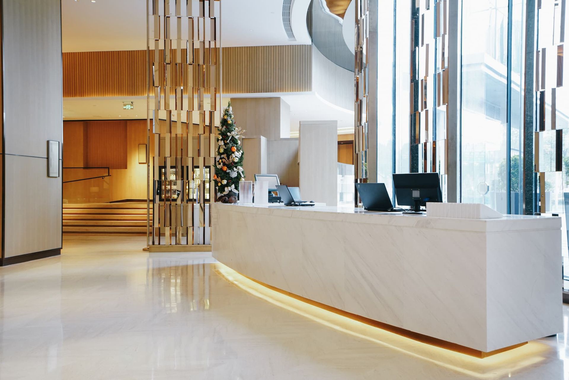 Modern hotel reception desk with a marble countertop, golden accents, and a small Christmas tree.