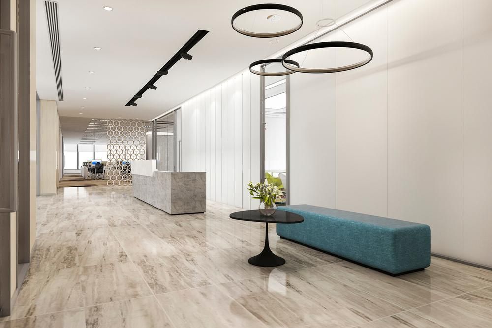 Modern office lobby with marble floors, a waiting bench, and a small table with flowers.