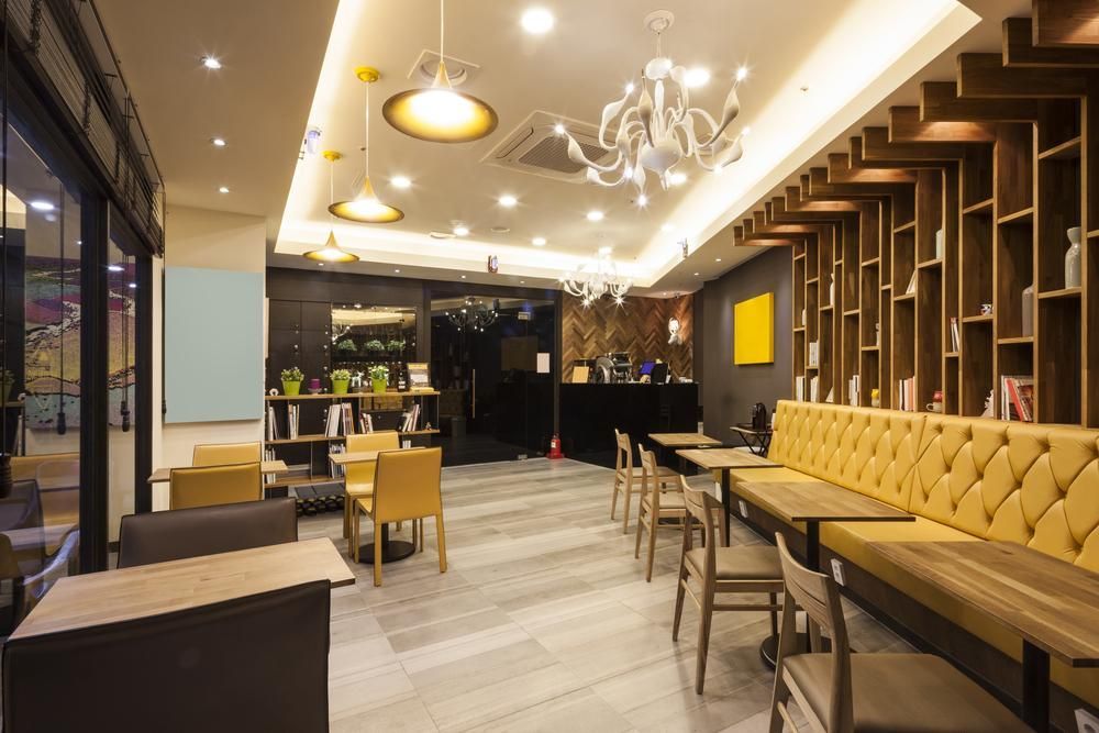 Interior of a cafe with yellow chairs and sofa, wooden shelves, and modern lighting.