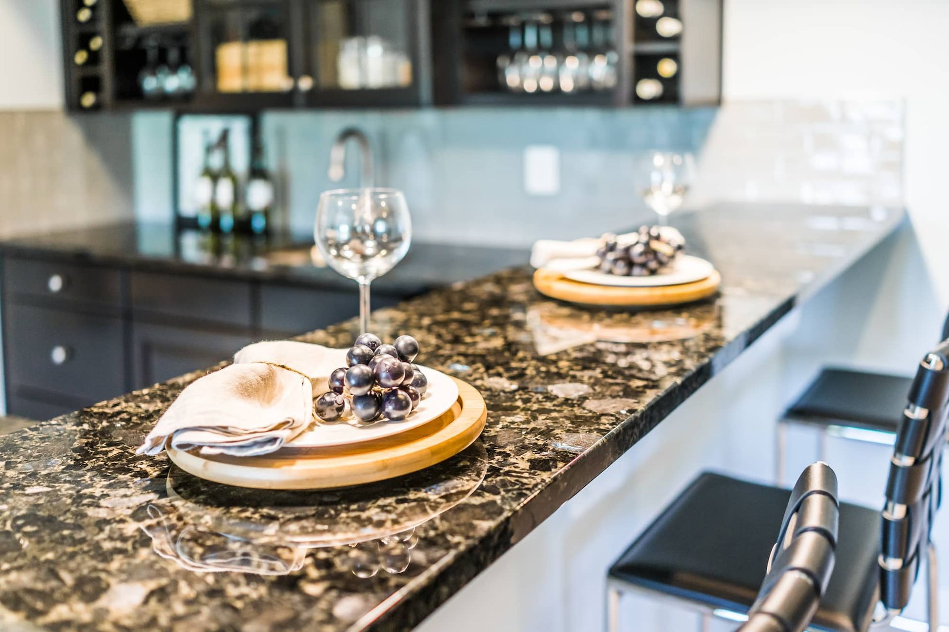 A home bar with granite countertop, wooden cabinets, and wine glasses set for a gathering.